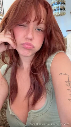 Woman with red hair in a green tank top, making a playful face indoors.