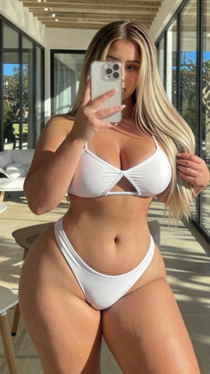 Woman in white bikini taking mirror selfie in modern indoor space.