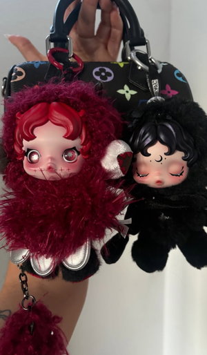 Two plush dolls attached to a patterned handbag.