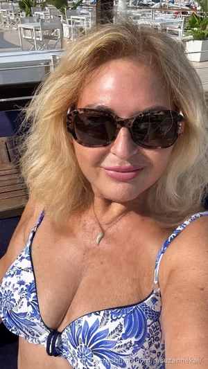 Blonde woman in blue floral bikini top, wearing sunglasses, outdoors near patio seating.