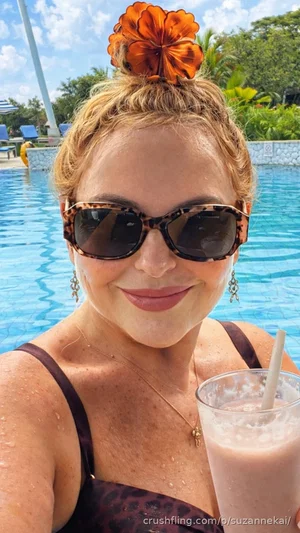 Woman in leopard print swimsuit with flower hair accessory, holding drink by pool.