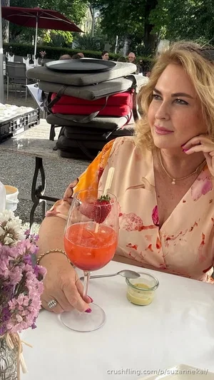 Woman with blonde hair in floral blouse holding cocktail at outdoor table.