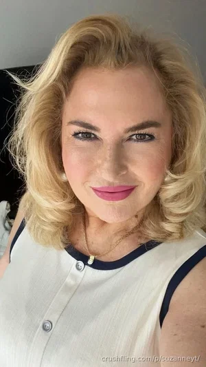 Blonde woman in white sleeveless top with navy trim, smiling in indoor setting.