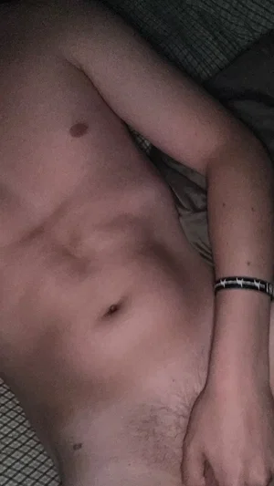 Shirtless man with toned torso lying on patterned surface, wearing black bracelet.