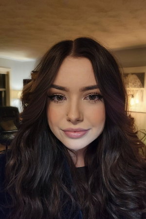 Brunette woman with long wavy hair, makeup, dark top, indoor.