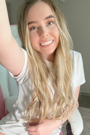 Blonde woman in white t-shirt taking selfie indoors.