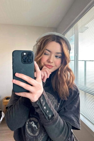 Woman taking selfie indoors wearing sweatshirt and headphones.