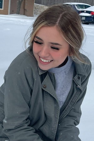 Blonde woman in green jacket smiling in snow.