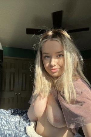 Blonde woman taking bedroom selfie with shirt lifted.