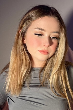 Blonde woman in gray top posing indoors.
