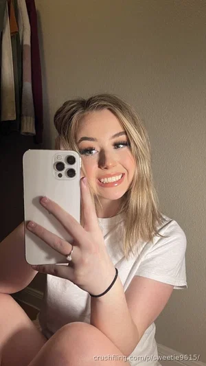 Woman with blonde hair in white t-shirt taking mirror selfie indoors.