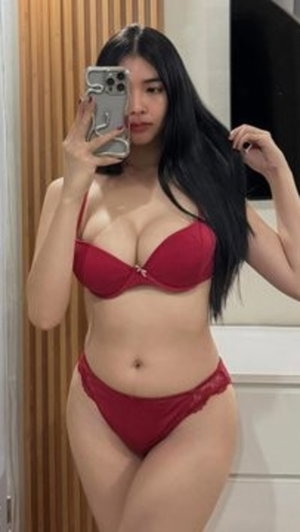 Woman with long black hair in red lingerie taking mirror selfie indoors.