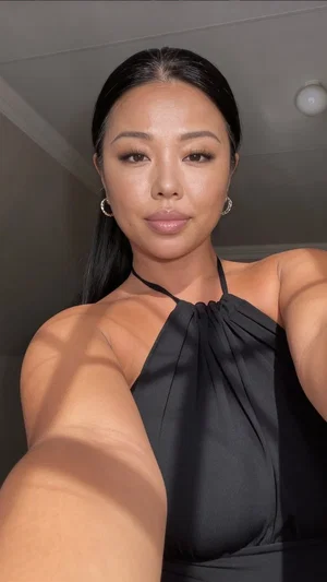 Woman with dark hair in black halter top taking mirror selfie indoors.