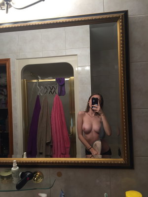 Woman with bare breasts and black underwear takes mirror selfie in bathroom.