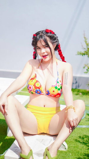 Woman in colorful bikini sitting outdoors on grass.
