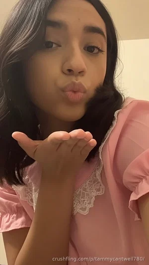 Woman with dark hair in pink lace-trimmed top blowing a kiss indoors.