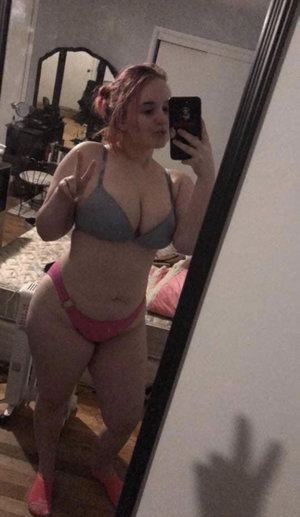Woman in gray bra and pink underwear takes mirror selfie in bedroom.