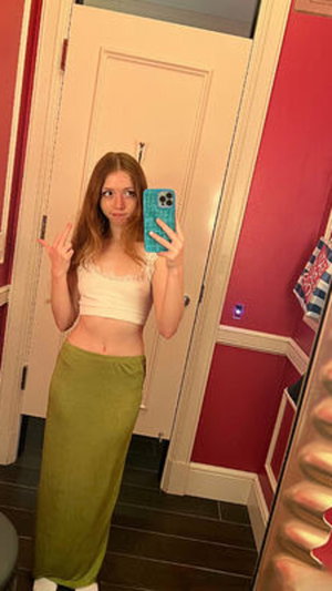 Slim redhead in white lace crop top and green skirt in bathroom.