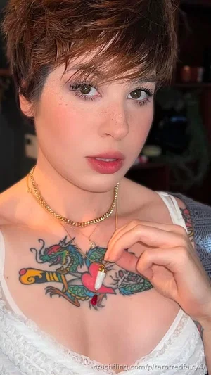 Woman with short brown hair, chest tattoo, white lace top, indoors.