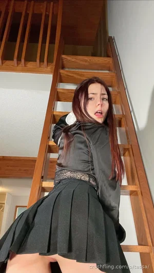 Woman in black schoolgirl outfit posing on wooden staircase indoors.