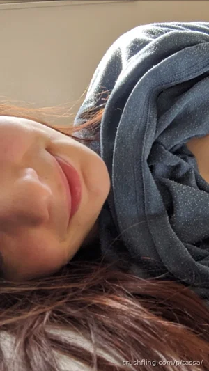 Woman with brown hair resting on a dark gray blanket, face partially visible, indoor setting.