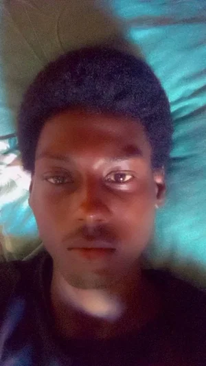 Black man with short hair lying on a teal pillow, wearing a dark shirt.