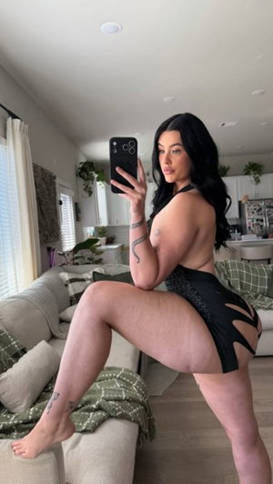 Woman in black cutout lingerie taking selfie in living room.