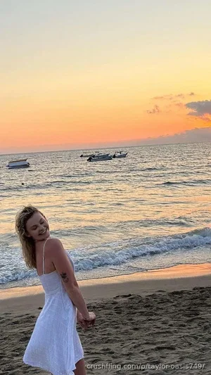 Woman in white dress on beach at sunset, facing away, smiling.