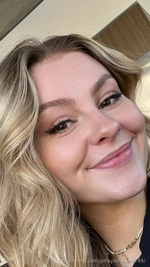 Blonde woman with wavy hair smiling in a close-up selfie indoors.