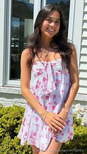 Woman in floral strapless dress standing outdoors near house and greenery.