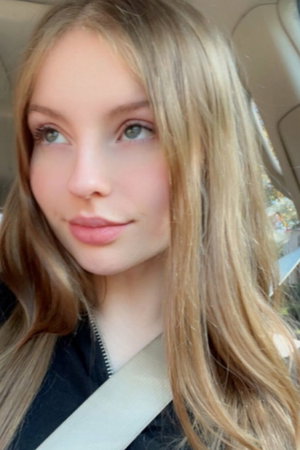 Blonde woman in black jacket in car with seatbelt.