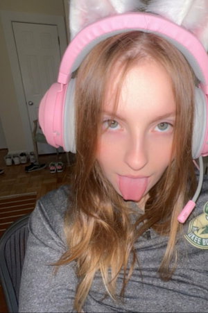 Slim woman with long brown hair in pink cat ear headphones and gray sweatshirt indoors.