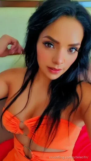 Woman with long black hair in orange cutout top, posing indoors.