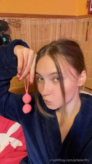 Woman in navy robe holding pink beads, indoor setting with bamboo backdrop.