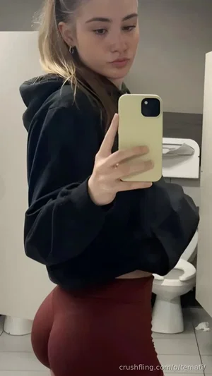 Woman in black hoodie and red pants takes mirror selfie in bathroom.