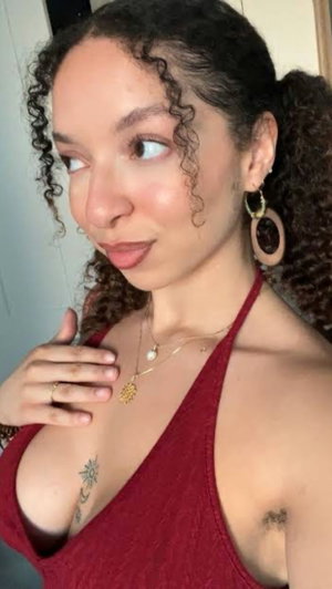 Woman with curly hair in red halter top taking selfie indoors.