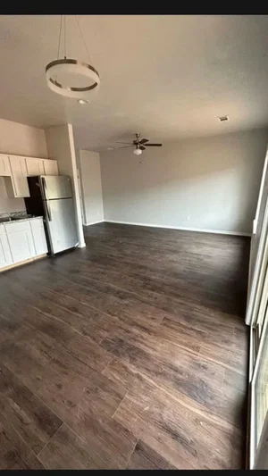 Empty room with wooden floors, white cabinets, and a refrigerator.