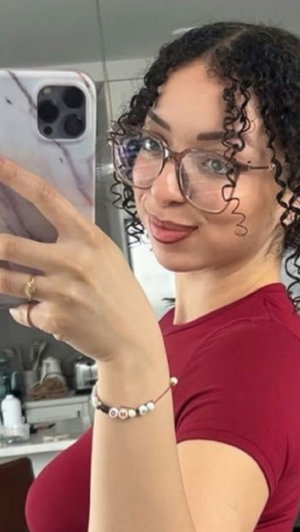 Woman with curly hair and glasses wearing red shirt taking selfie indoors.