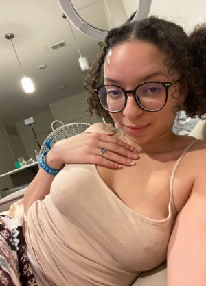 Curvy woman with curly hair and glasses in beige tank top indoors.