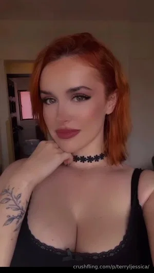 Woman with red hair and black lace top, wearing choker, indoors.