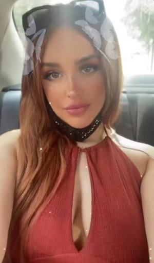 Curvy woman with auburn hair in red halter top in car.
