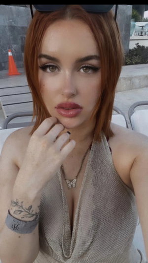 Red-haired woman in beige halter top posing outdoors.