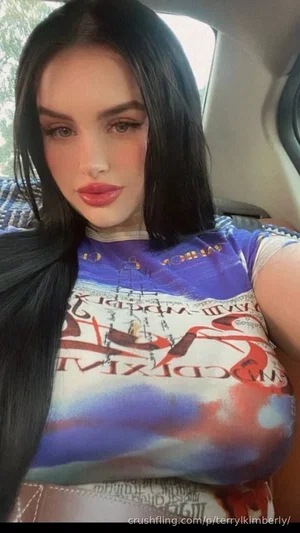 Woman with long black hair wearing colorful graphic top, sitting in car.