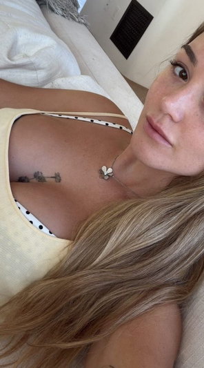 Blonde woman in yellow top taking selfie on bed.