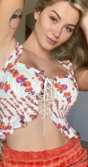 Blonde woman in floral lace-up top and orange skirt indoors.