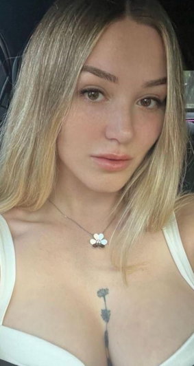 Blonde woman in white top with necklace and tattoo.