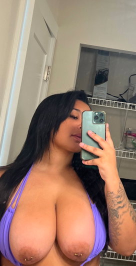Curvy woman in purple bikini taking bathroom mirror selfie.