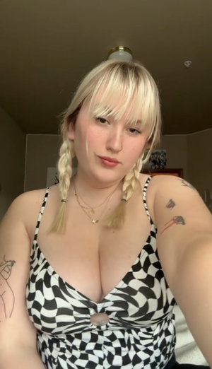 Woman with blonde braids in black and white checkered top, indoor selfie.