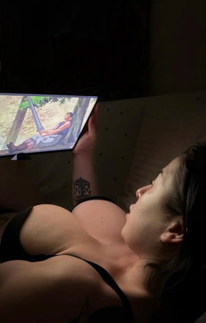 Woman in black bra lying on bed holding tablet.