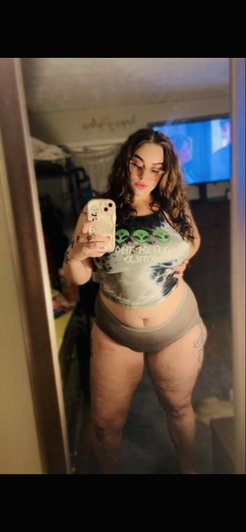 Woman in crop top and underwear taking mirror selfie in bedroom.
